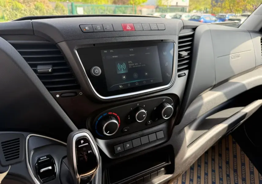 Vue rapprochée de la console centrale et levier de vitesse automatique du tableau de bord noir du Iveco Daily blanc 2026.
