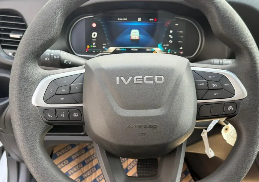 Vue rapprochée du volant noir de l’Iveco Daily 2026 avec commandes intégrées et tableau de bord numérique en arrière-plan.
