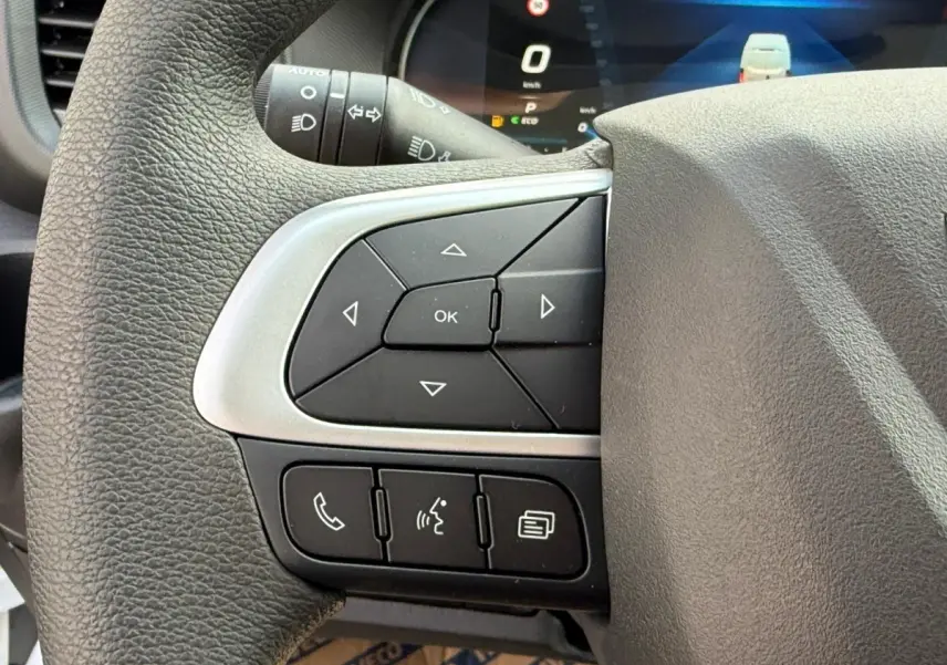 Gros plan sur les commandes multifonctions à gauche du volant du Iveco Daily blanc 2026, avec affichage numérique en arrière-plan.
