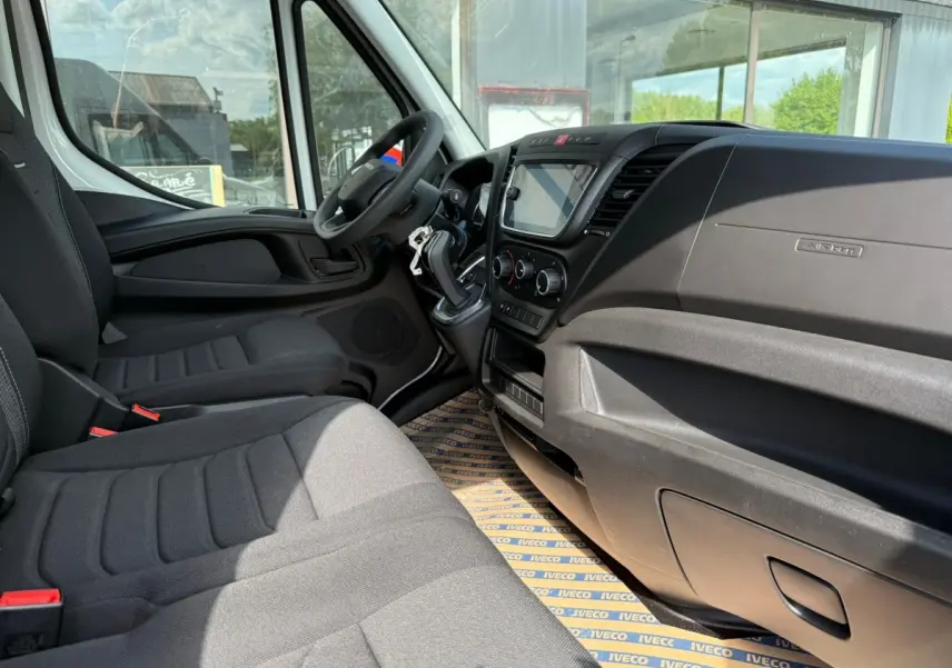 Vue intérieure côté conducteur de l’Iveco Daily blanc 2026, montrant le tableau de bord et les sièges en tissu gris.