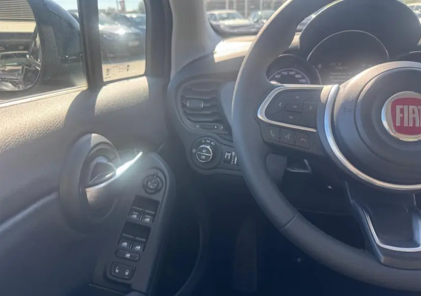 Vue intérieure côté conducteur du Fiat 500X bleu, montrant le volant, commandes des vitres et rétroviseurs.