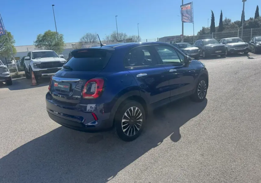 Vue 3/4 arrière droite d'une FIAT 500X bleu foncé avec jantes classiques 16 pouces, stationnée en extérieur.