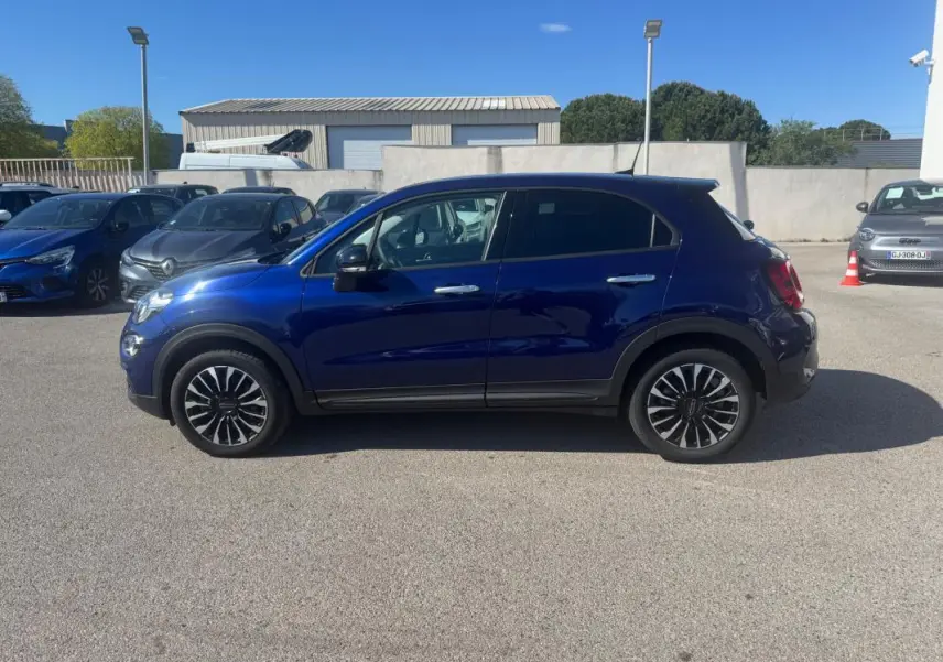 Profil droit d'un FIAT 500X bleu MY23 avec jantes classiques 16 pouces sur parking extérieur ensoleillé.