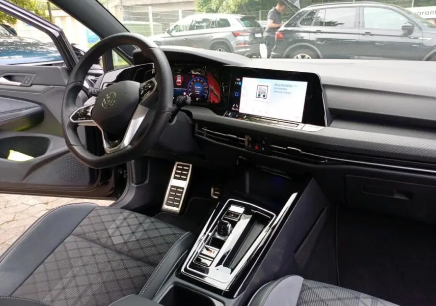 Vue intérieure côté conducteur de la Volkswagen Golf 1.5 eTSI 2024 avec tableau de bord digital et sellerie tissu noir à motifs.