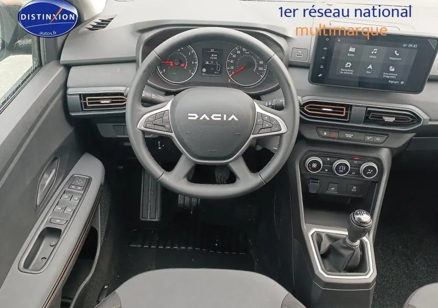 Vue intérieure du poste de conduite de la Dacia Sandero 2025 avec volant multifonction, écran tactile et levier de vitesse manuel.