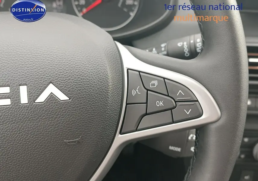 Gros plan sur les commandes au volant à droite du Dacia Sandero noir, montrant les boutons multifonctions et le logo partiel.