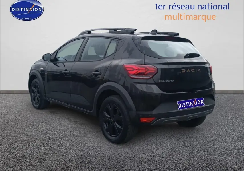 Vue 3/4 arrière droite d'une Dacia Sandero noire avec barres de toit et jantes noires sur fond neutre.