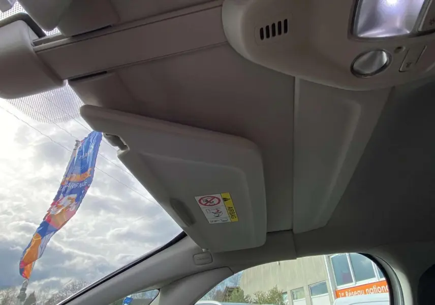 Vue intérieure côté conducteur du pare-soleil relevé et du plafond clair du Citroën Grand C4 Picasso blanc 2015.