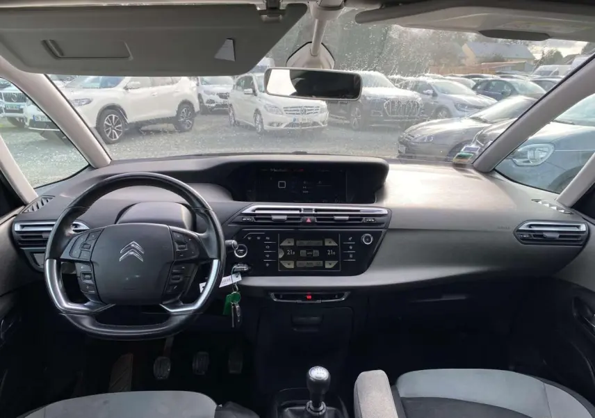 Intérieur du Citroën Grand C4 Picasso blanc 2015, vue frontale du tableau de bord avec volant cuir et boîte manuelle.