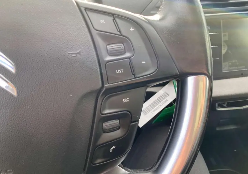 Gros plan sur le volant cuir noir du Citroën Grand C4 Picasso 2015, avec commandes audio intégrées et écran tactile en arrière-plan.