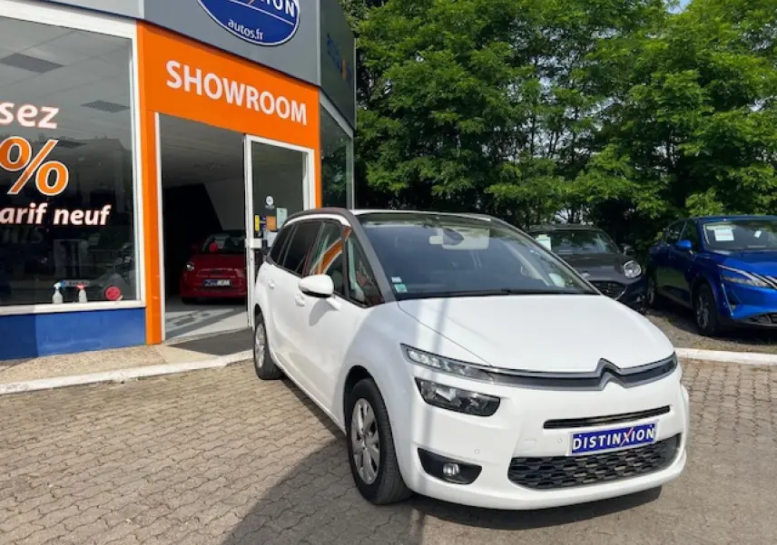 Vue 3/4 avant d'un Citroën Grand C4 Picasso blanc garé devant un showroom avec toit panoramique noir.