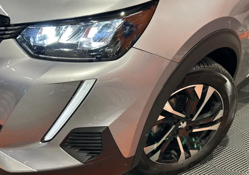 Gros plan sur l’avant droit gris Artense du Peugeot 2008 avec phare LED allumé et jante alliage bicolore.