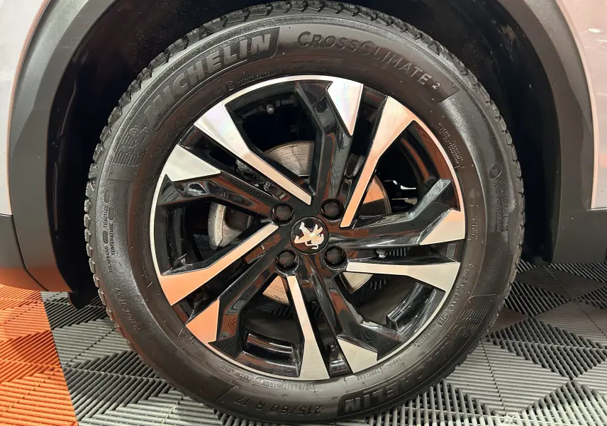Gros plan sur la roue avant droite d’un Peugeot 2008 gris Artense avec jante alliage bicolore et pneu Michelin CrossClimate.