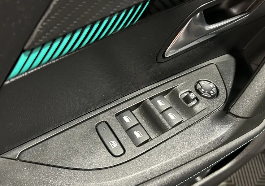 Détail des commandes de lève-vitres et rétroviseurs côté conducteur, intérieur noir avec surpiqûres bleues.