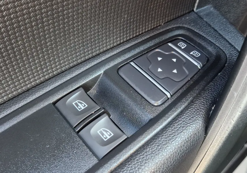 Gros plan sur les commandes des vitres et rétroviseurs électriques côté conducteur d’un Renault Kangoo blanc 2024.