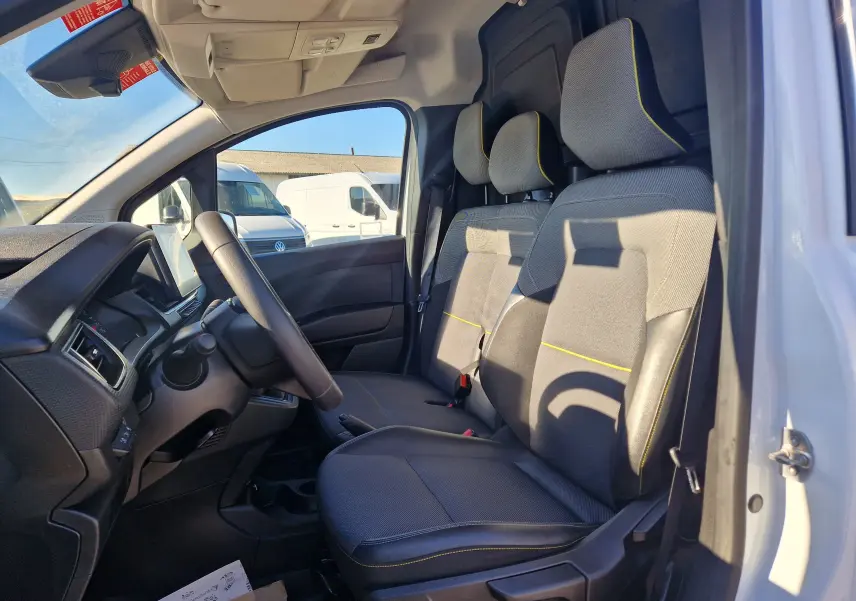 Vue intérieure côté conducteur du Renault Kangoo blanc 2024, montrant les sièges gris avec surpiqûres jaunes et le tableau de bord.