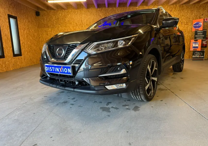 Vue 3/4 avant droit d'un Nissan Qashqai noir avec jantes alliage et calandre chromée dans un garage en bois.