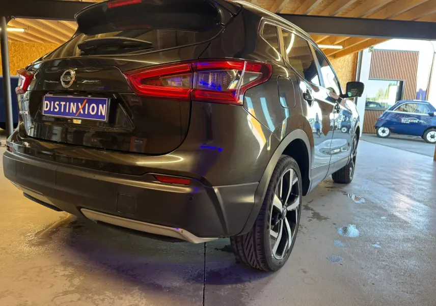 Vue 3/4 arrière droite du Nissan Qashqai noir avec jantes alu et barres de toit, stationné en intérieur lumineux.