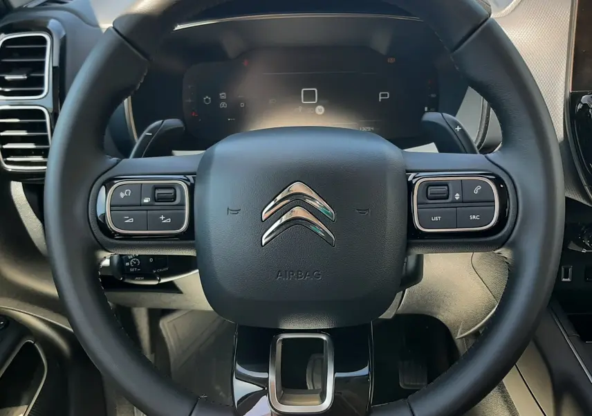 Vue rapprochée du volant noir du Citroën C5 Aircross Ph.2 Hybrid 145ch, avec commandes intégrées et tableau de bord numérique.