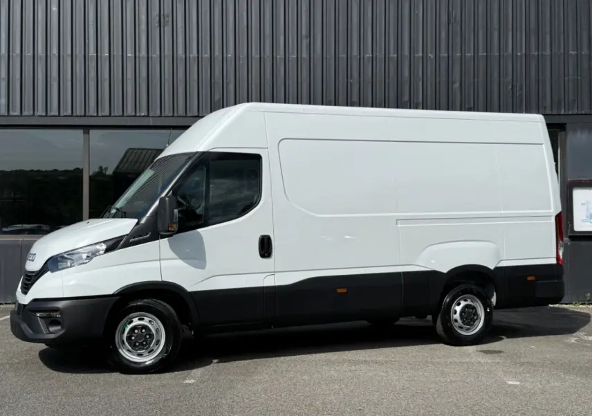 Vue de profil côté gauche d’un utilitaire Iveco Daily blanc avec bas de caisse noir, sans marquages, sur fond industriel.