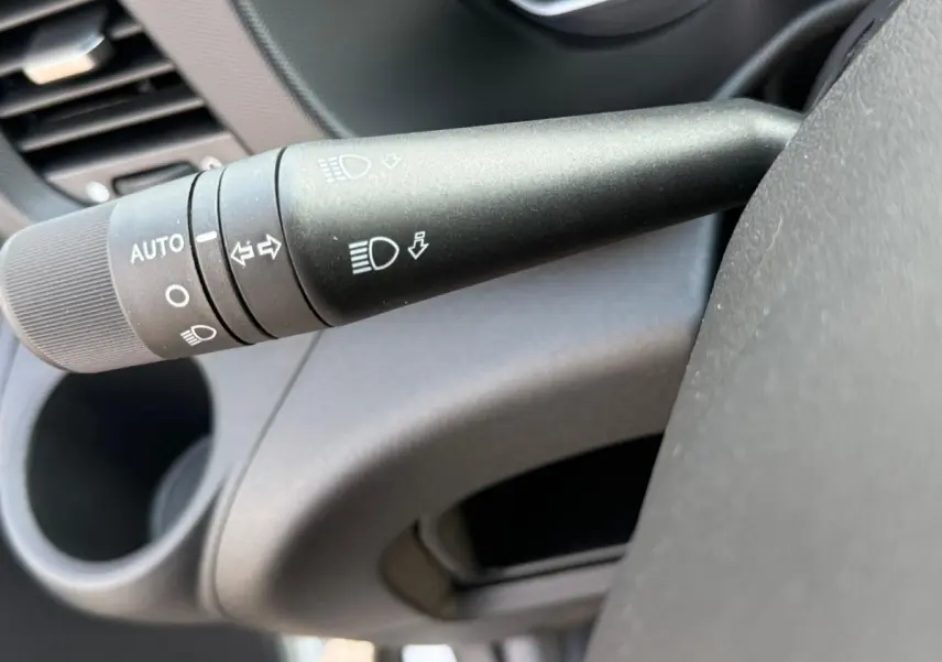 Gros plan sur la commande des phares et clignotants à gauche du volant dans l’habitacle gris de l’Iveco Daily blanc.