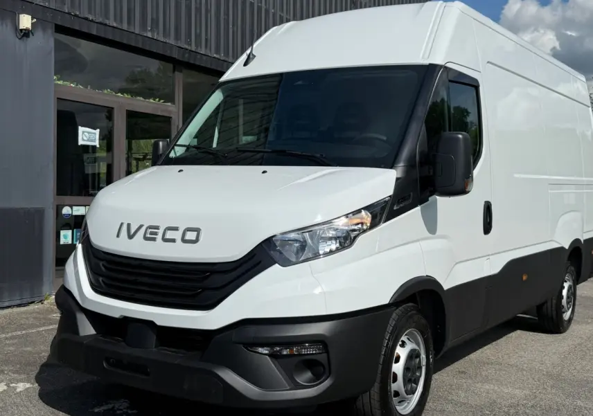 Vue 3/4 avant d’un utilitaire Iveco Daily blanc avec calandre noire et pare-chocs noir, stationné devant un bâtiment.