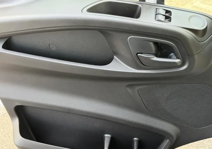 Vue rapprochée de la porte intérieure côté conducteur de l'Iveco Daily 2026, avec poignée, commandes de vitres et rangement noir.