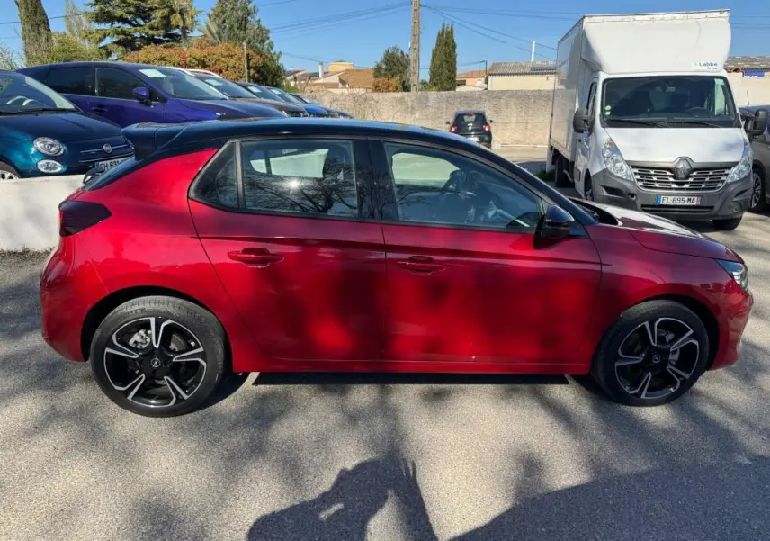 Vue de profil côté gauche d'une Opel Corsa rouge 2025 avec jantes noires et toit noir, garée en extérieur.