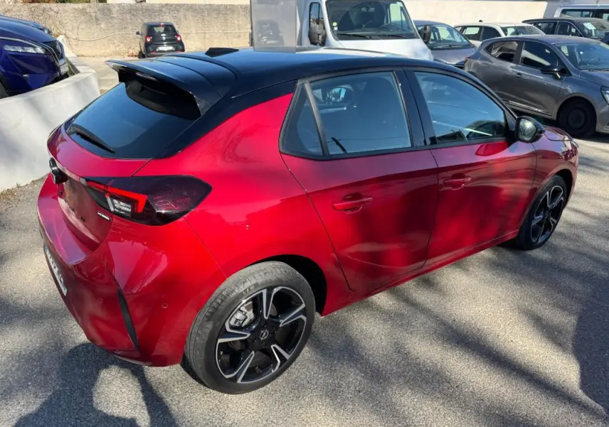 Vue 3/4 arrière droite d'une Opel Corsa rouge 2025 avec toit noir et jantes alliage noires distinctives.