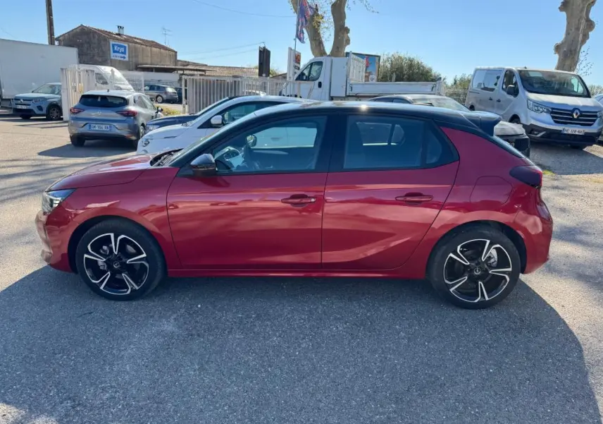 Vue latérale côté gauche d'une Opel Corsa 1.2 Turbo Hybrid rouge 2025 avec toit noir et jantes noires à motifs argentés.