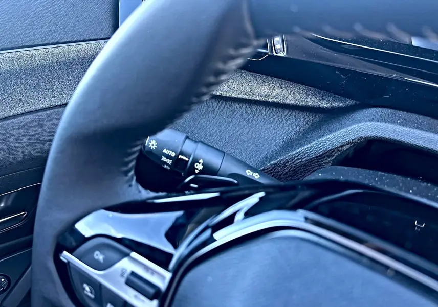 Gros plan sur le volant noir et la commande des phares du Peugeot 308 1.5 BlueHDi 130 Allure 2025.
