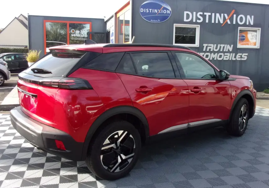 Vue 3/4 arrière droite d'un Peugeot 2008 2024 rouge Elixir avec toit noir et jantes alliage modernes.