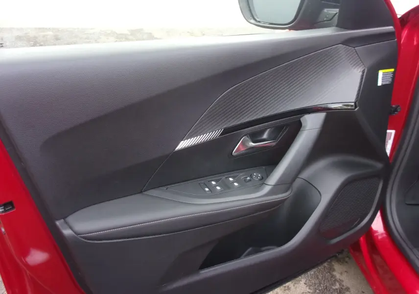 Porte avant gauche ouverte d'un Peugeot 2008 rouge Elixir, montrant le panneau intérieur noir avec insert texturé et commandes électriques.
