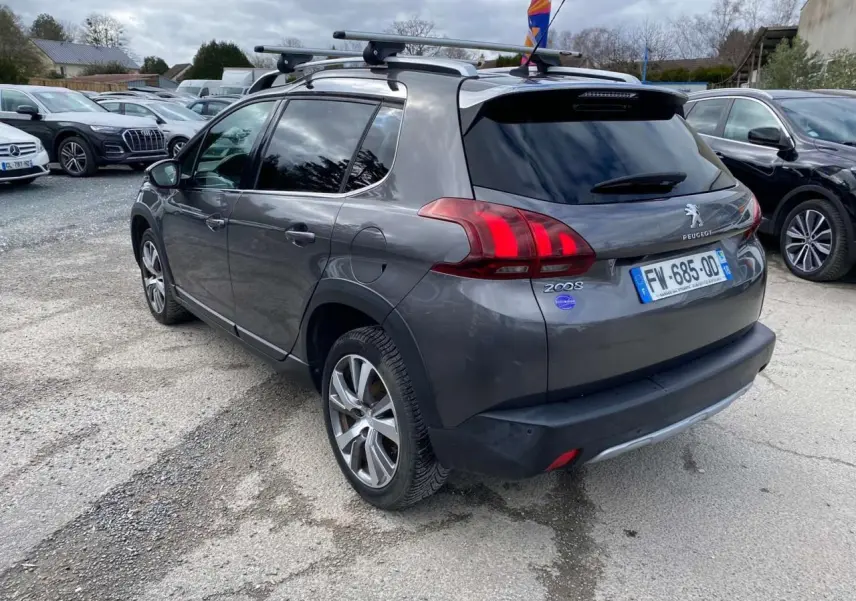 Peugeot 2008 gris platinium vue 3/4 arrière droit avec barres de toit aluminium et vitres teintées.