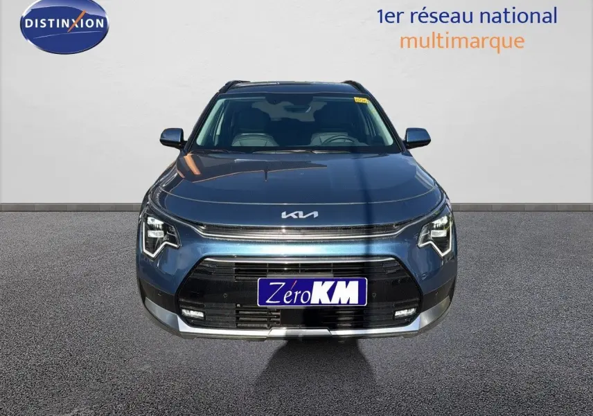 Vue frontale d'un KIA NIRO bleu minéral métal 2025 avec calandre noire et phares LED distinctifs allumés.