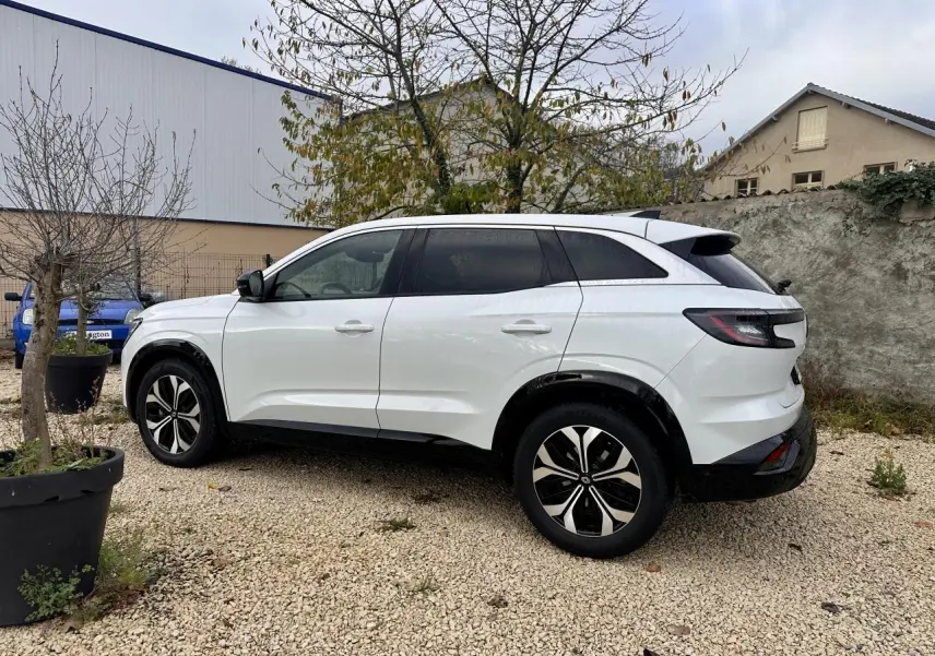 Renault Austral blanc en vue profil côté gauche, stationné sur gravier avec jantes noires et toit noir contrasté.