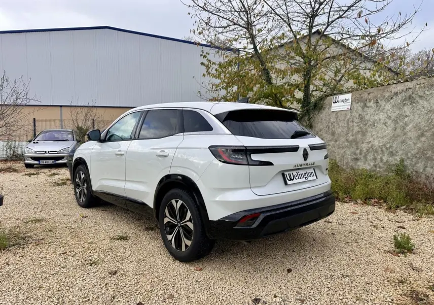 Renault Austral blanc vu en 3/4 arrière droit, avec feux arrière LED et vitres teintées sur terrain gravillonné.