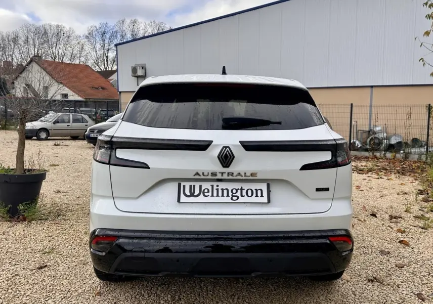 Vue arrière d'un Renault Austral blanc avec feux arrière étirés et logo central sur fond urbain.