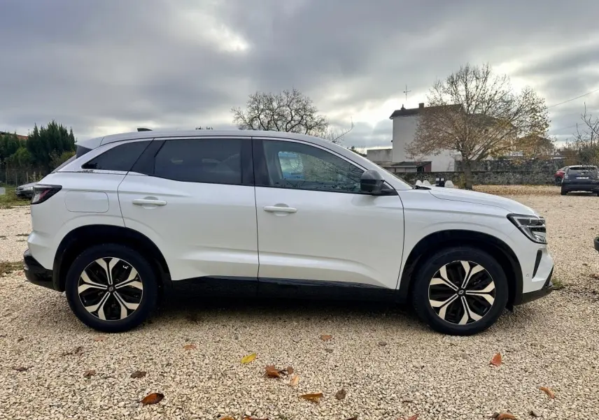 Profil côté gauche d'un Renault Austral blanc 2024 avec jantes noires et toit noir sur fond de ciel nuageux.