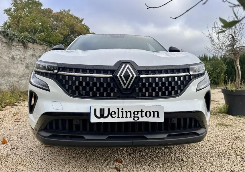 Vue frontale rapprochée d'un Renault Austral blanc avec calandre noire à motif géométrique et logo central proéminent.