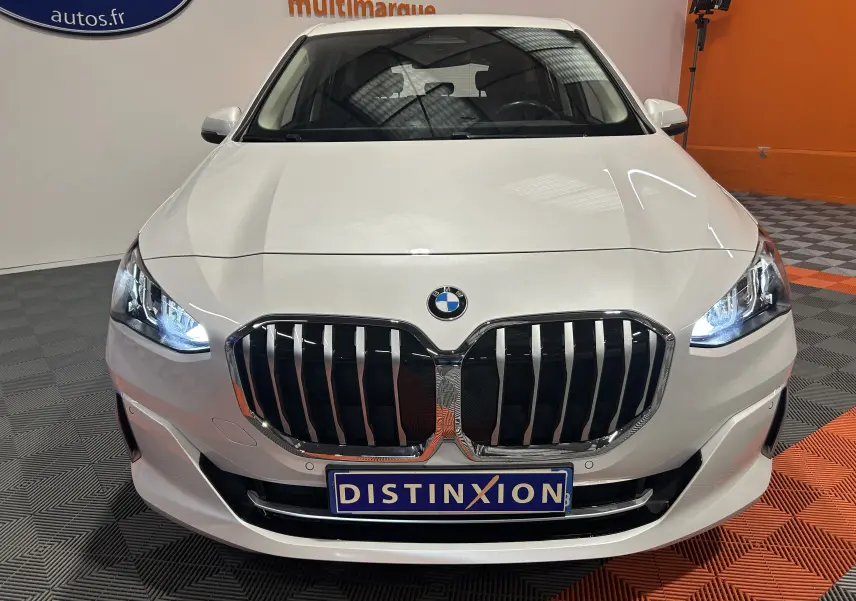 Vue avant d'une BMW Série 2 Active Tourer blanche avec calandre imposante et phares allumés en intérieur showroom.