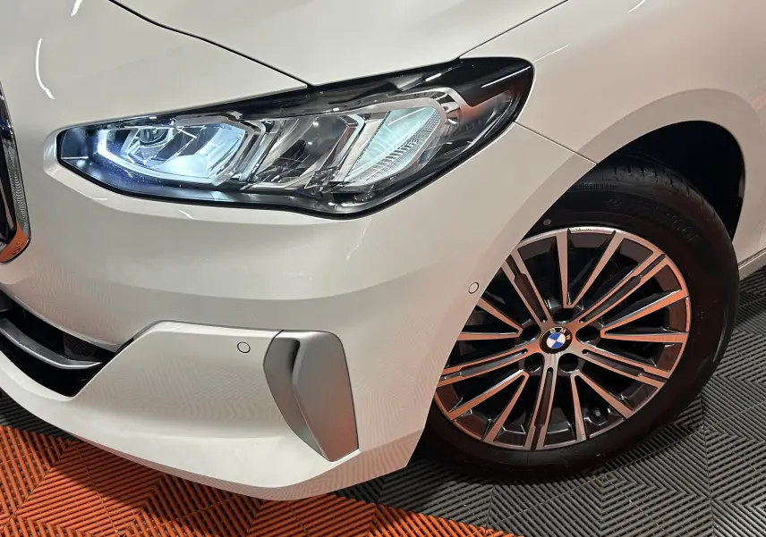 Gros plan sur l'avant droit blanc métallisé d'une BMW Série 2 Active Tourer 218i avec phare LED et jante alliage multibranches.