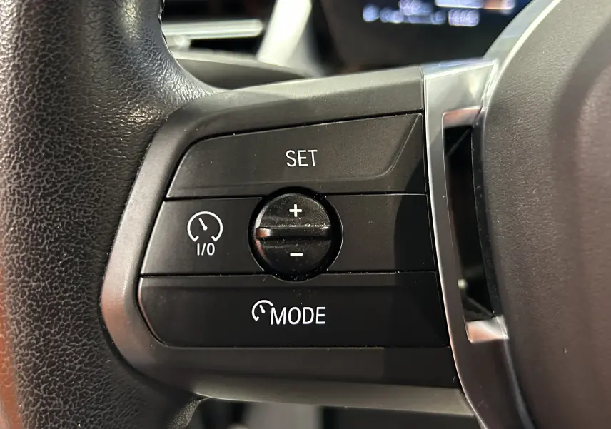 Gros plan sur les commandes de régulateur de vitesse au volant d’une BMW Série 2 Active Tourer blanche.