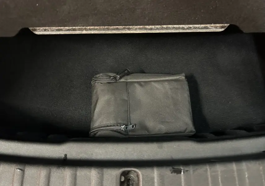 Vue plongeante sur le coffre ouvert d'une BMW Série 2 Active Tourer blanc, avec une trousse noire zippée à l'intérieur.