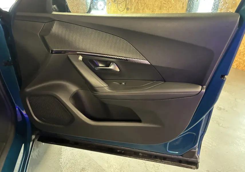 Vue intérieure de la porte avant gauche bleu Peugeot 2008 1.2 Hybrid 136 Allure avec garniture noire et insert carbone.