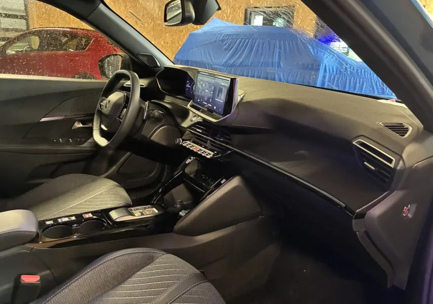Vue intérieure côté conducteur du Peugeot 2008 1.2 Hybrid 136 Allure 2025 avec tableau de bord noir et écran tactile central.