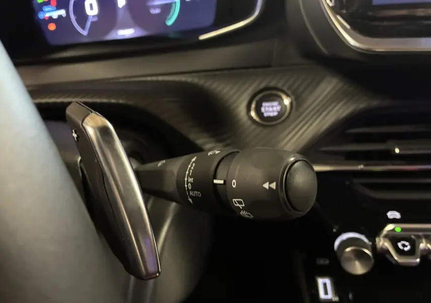 Gros plan sur la commande d’essuie-glace et palette de changement de vitesse dans l’habitacle noir du Peugeot 2008 hybride 2025.