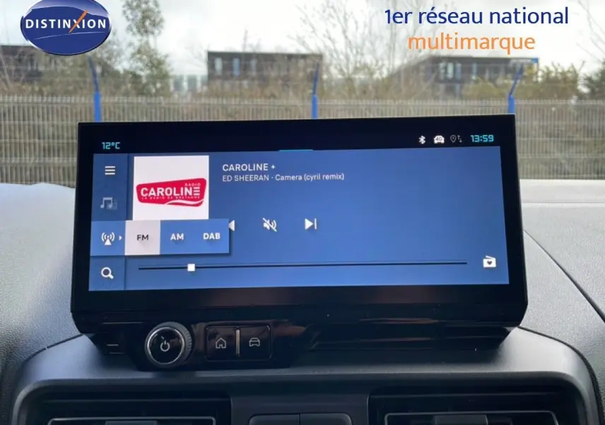 Écran tactile central du tableau de bord du Citroën Berlingo blanc, affichant une radio FM avec station Caroline.