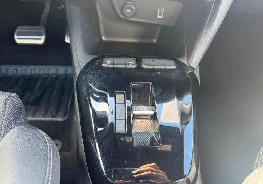 Gros plan sur la console centrale noire brillante de l’Opel Corsa 1.2 Turbo Hybrid 2025 avec levier de boîte automatique et boutons de contrôle.