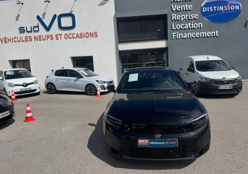 Opel Corsa 1.2 Turbo Hybrid noir vue de face, stationnée devant un concessionnaire avec d'autres véhicules autour.
